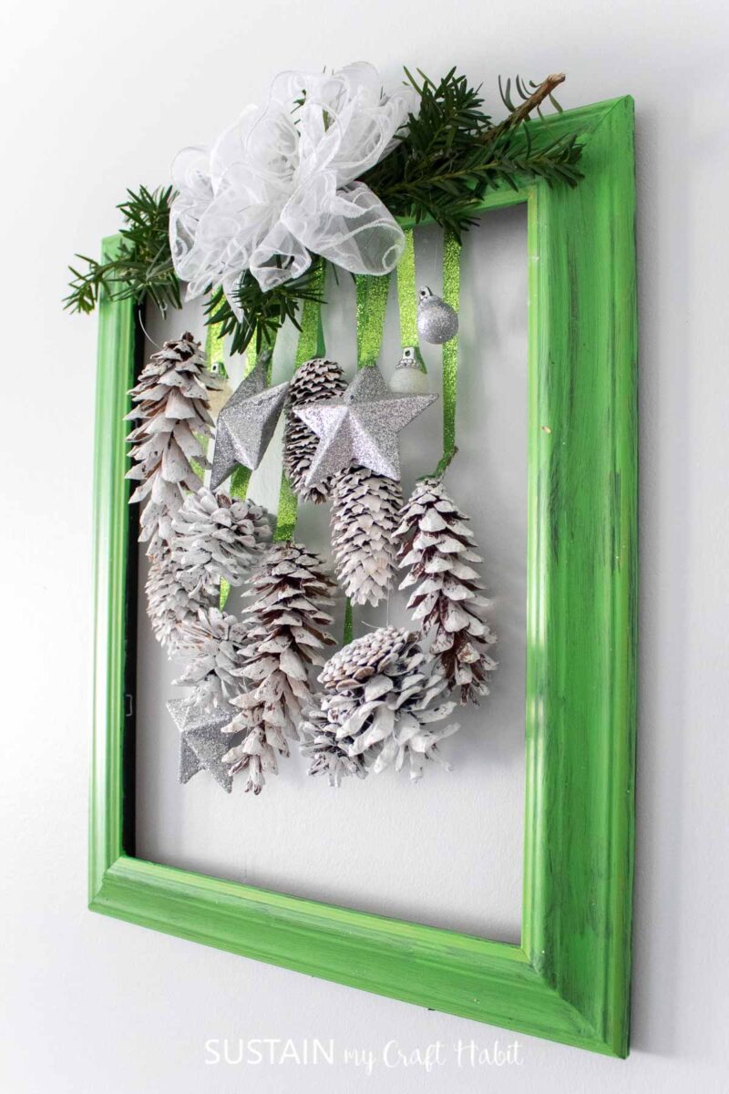 Upcycled picture frame door decor for the holidays with greenery, pine cones and ornaments.