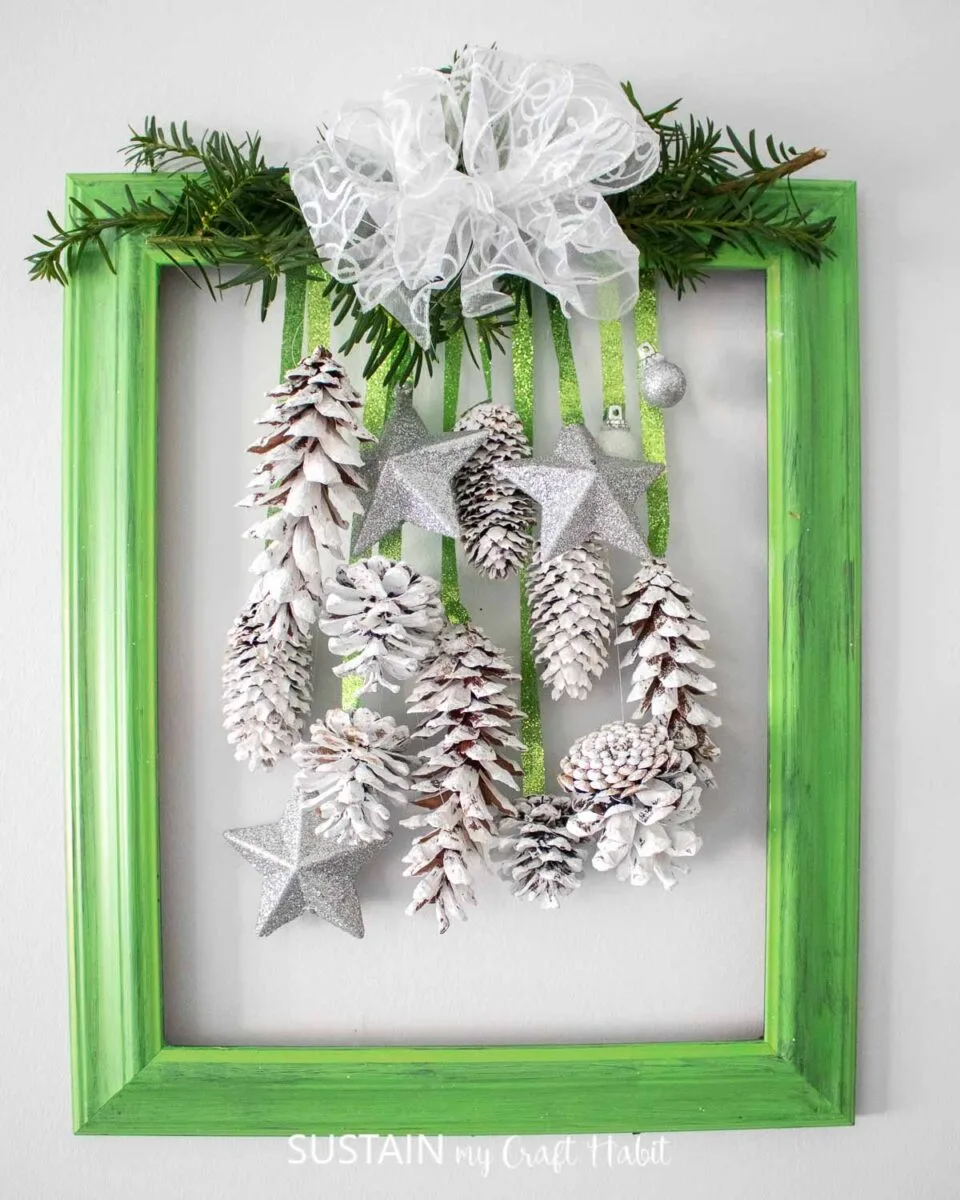 Upcycled picture frame door decor for the holidays with greenery, pine cones and ornaments.