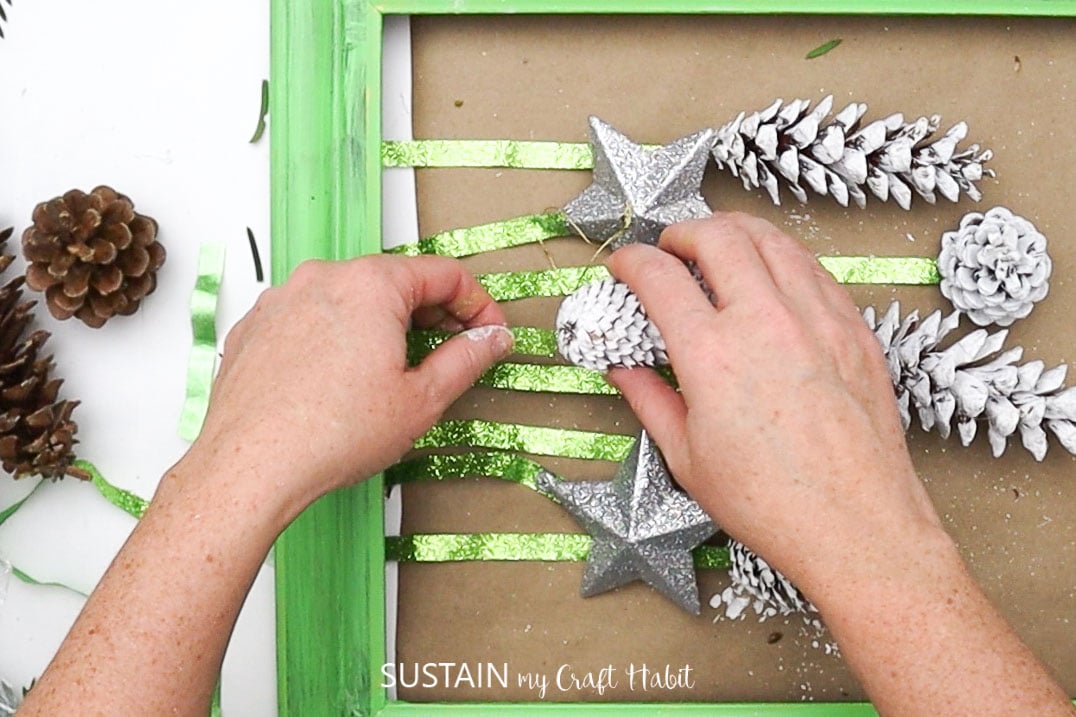 Attaching painted pine cones to ribbon.