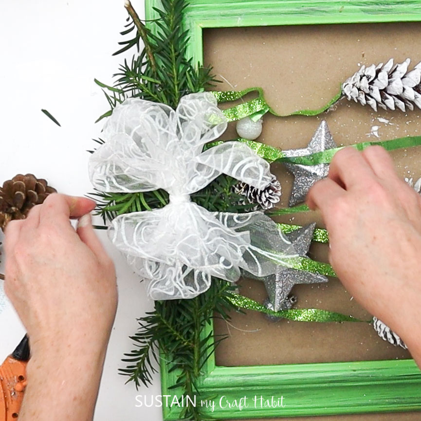 Attaching a bow to the greenery on the picture frame.