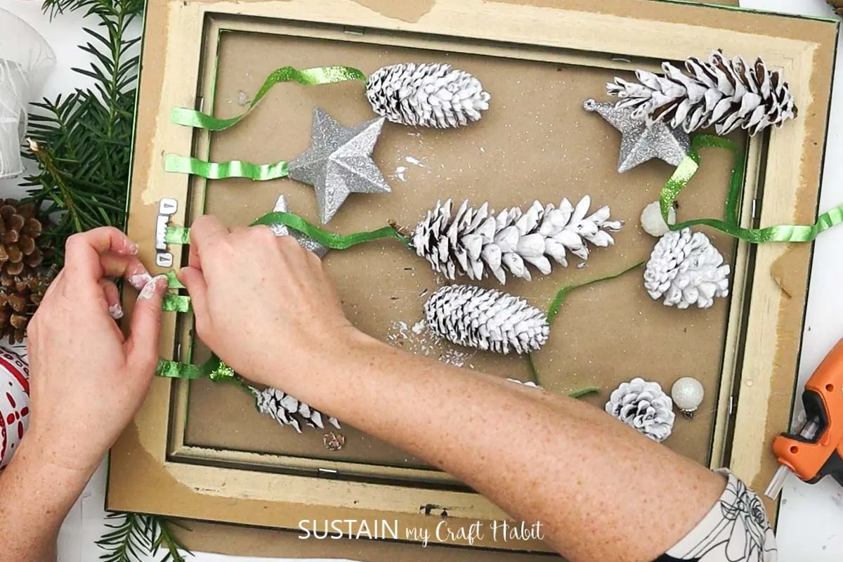 Attaching green ribbon to the back of the painted picture frame.