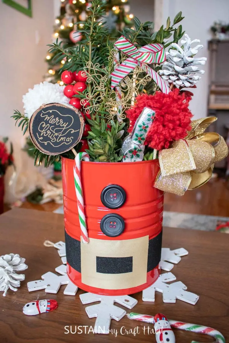 Coffee tin Santa centerpiece filled with greenery, bows, ribbon and festive embellishments.