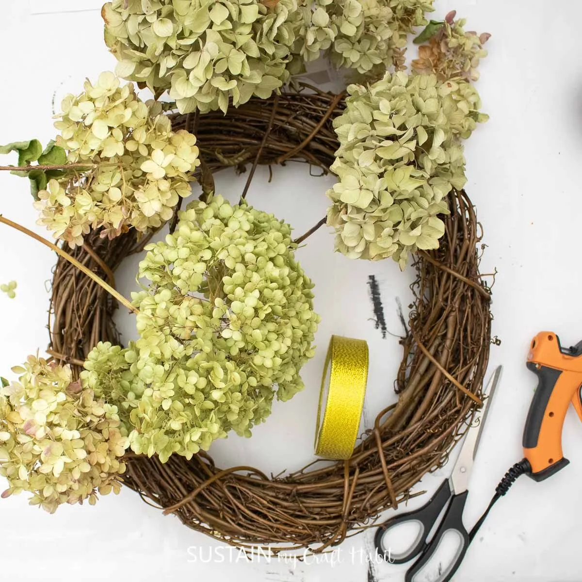 Materials needed to make a dried hydrangea wreath including dried hydrangea flowers, wreath form, ribbon and glue.
