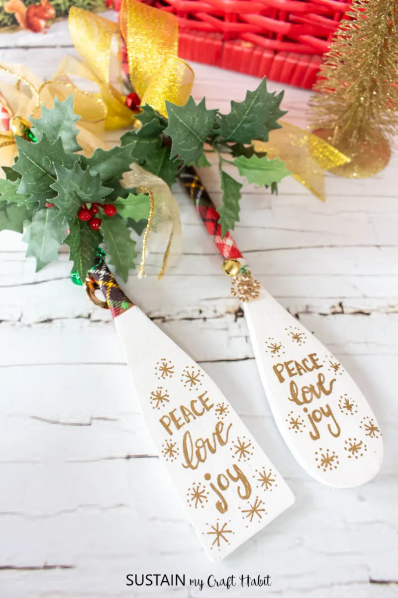Decorated wooden spoons with ribbon, greenery, bells and written festive greeting.