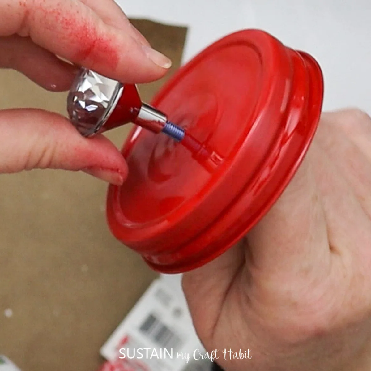 Attaching a decorative knob to the mason jar lid.