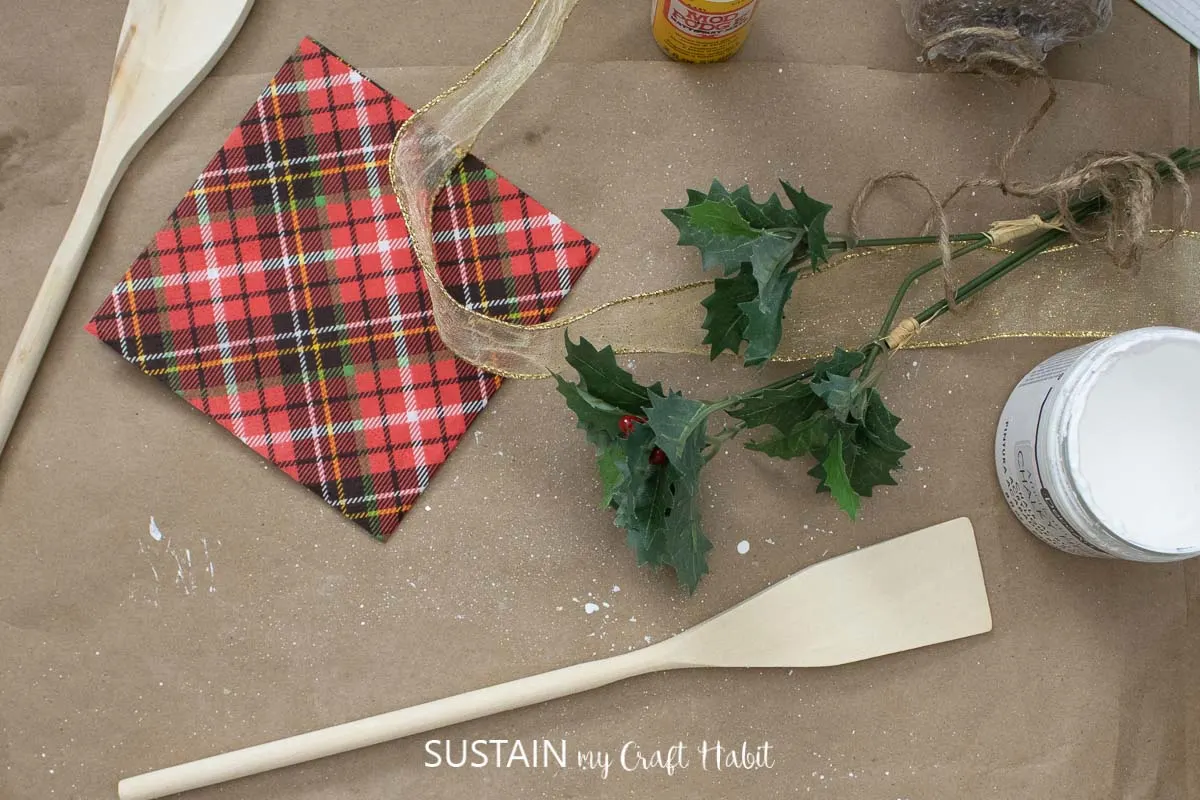 Materials needed to make decorated wooden spoons including wooden spoons, paint, napkins, ribbon, greenery, and mod podge.