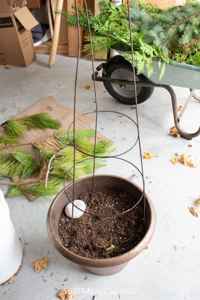 Filling a planter pot with soil and a tomato cage.