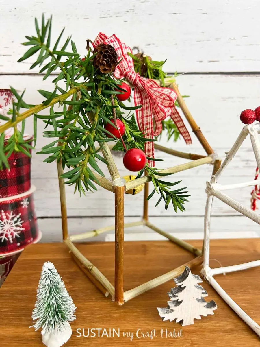 Rustic twig house decorations for Christmas embellished with greenery, pine cones and ribbon.