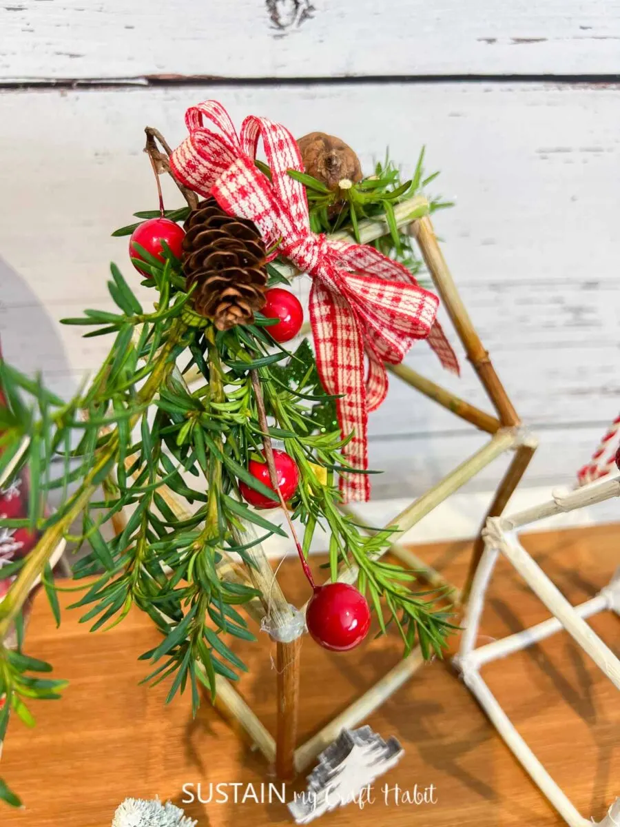 Top view of rustic twig house decorations for Christmas embellished with greenery, pine cones and ribbon.