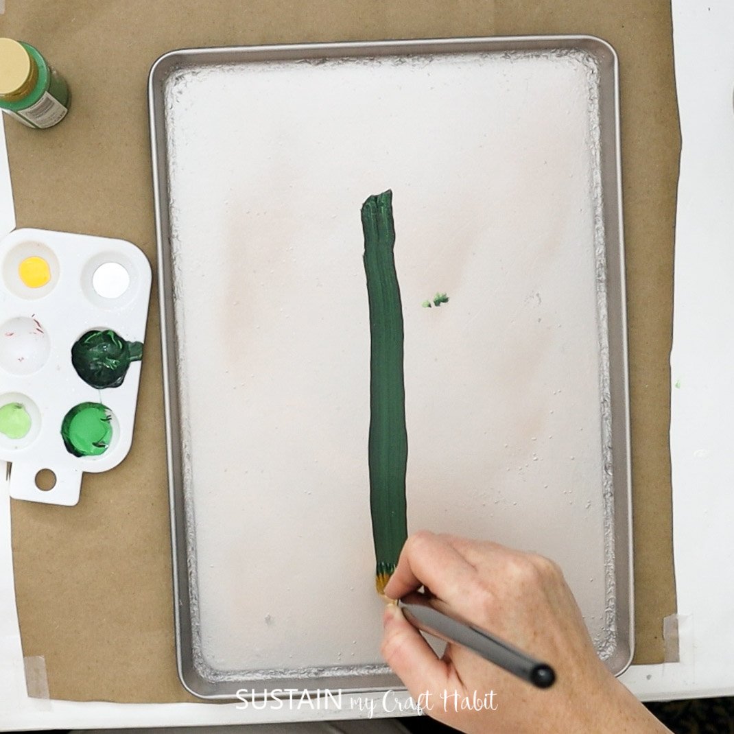 Painting a line of green paint on a cookie sheet.