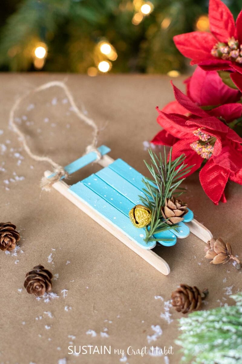 Popsicle stick sled ornament next to mini pine cones and poinsettia. 
