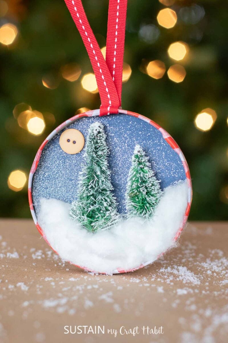 Bottle brush jar lid ornament with mini trees, fake snow a button.