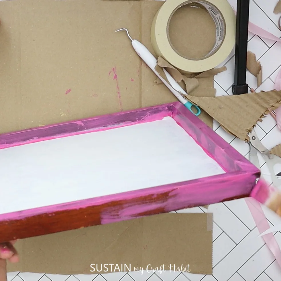 Painting the outside of the wood plaque with pink paint.