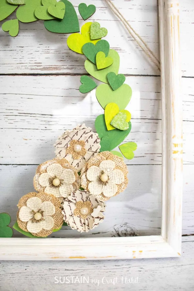 Close up of the wood heart cutout wreath in an upcycled picture frame with faux flowers.
