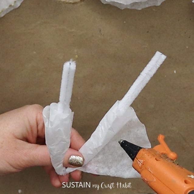 Hot gluing a coffee filter around a pipe cleaner.