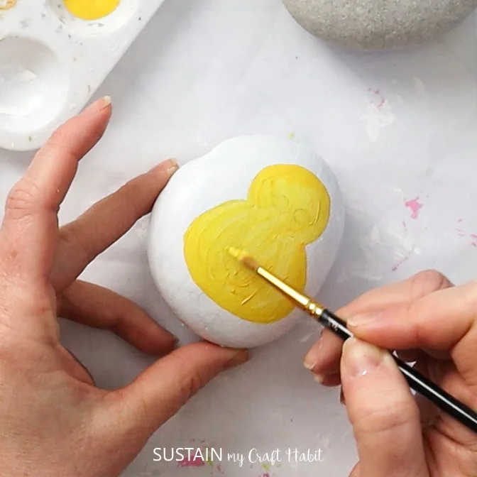 Painting a yellow baby chick onto a rock.
