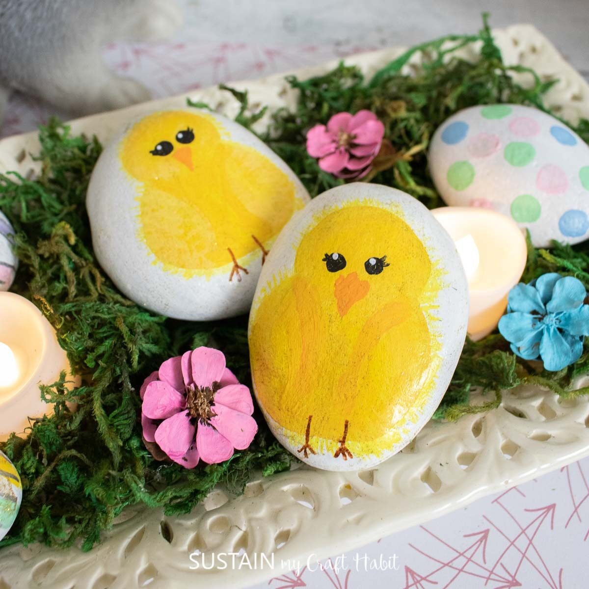 Easter rock painted baby chicks and Easter eggs placed on decorative plate with moss.