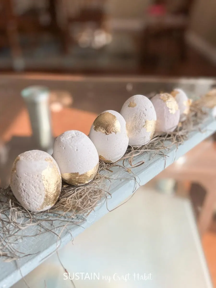 Cement eggs covered in gold foil and placed on a wooden paddle.