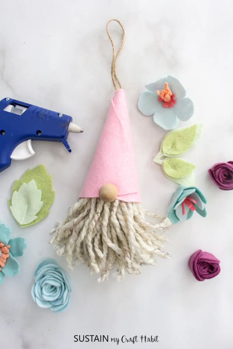 Gnome ornaments next to felt flowers and a hot glue gun.