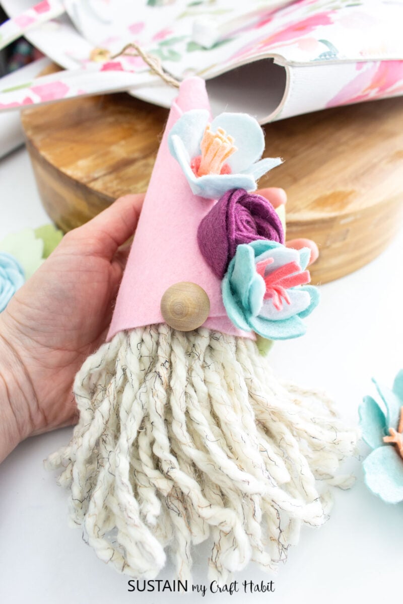 Hand holding a finished spring gnome ornament with a pink hat and felt flower embellishments. 