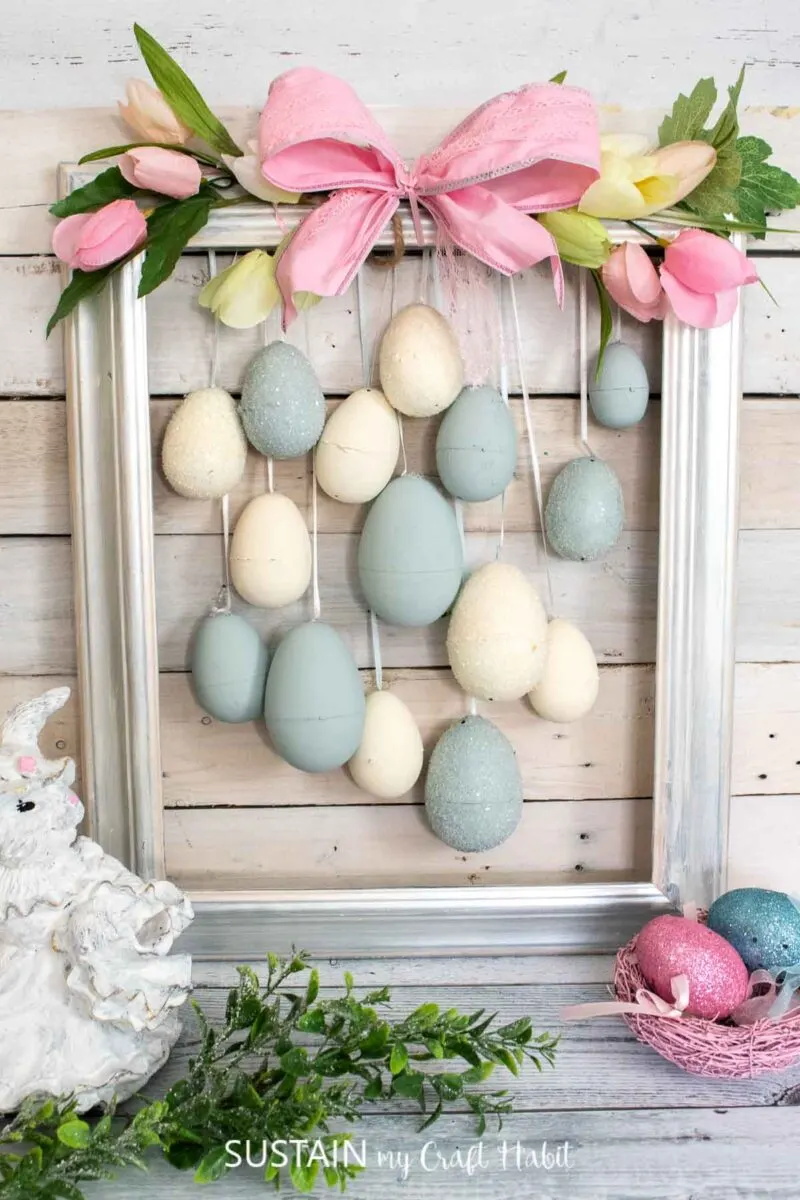 Painted plastic Easter eggs hung with ribbon onto an upcycled picture frame decorated with with faux tulips and a bow.