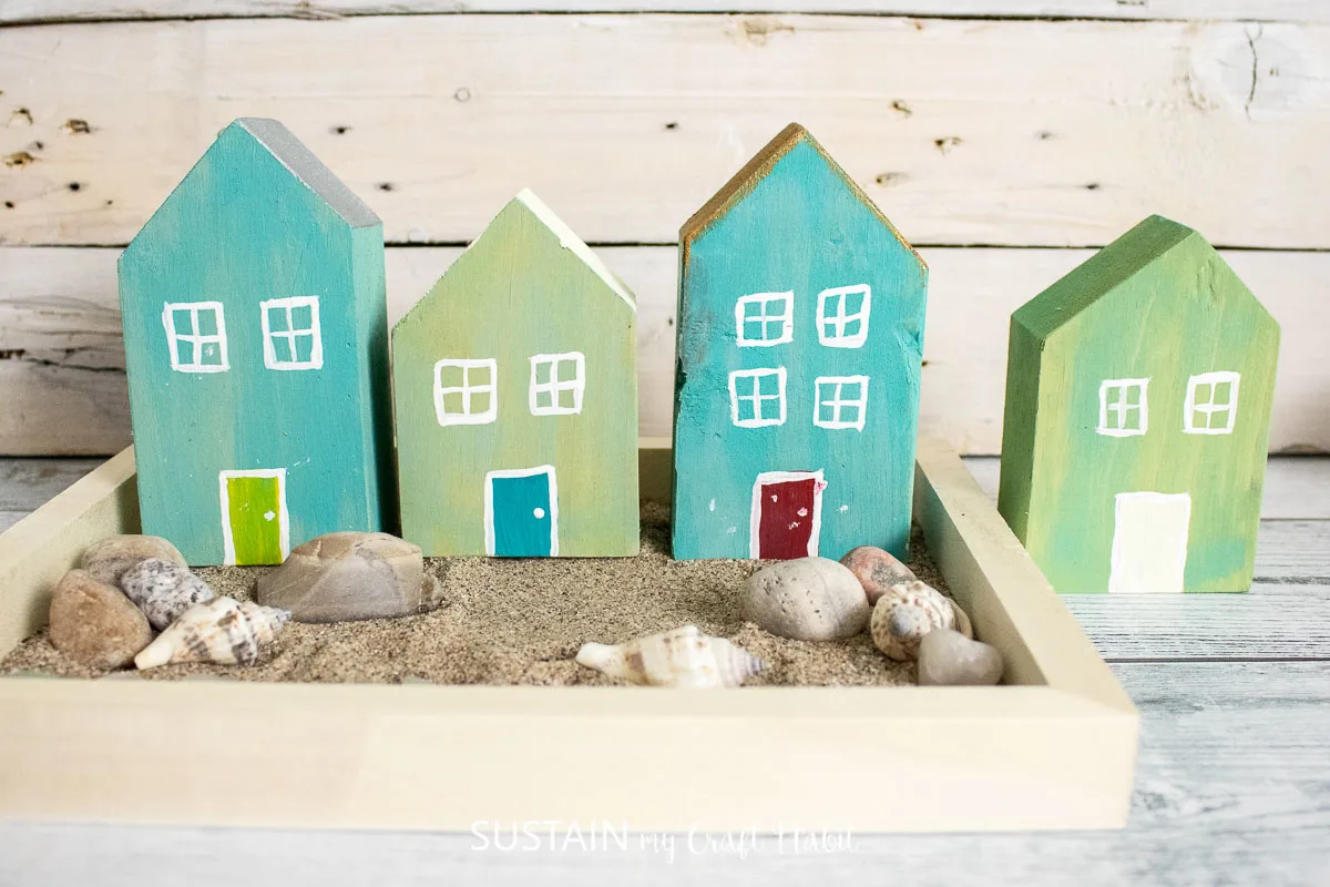 Scrap wood houses placed in sand, seashells and stones.