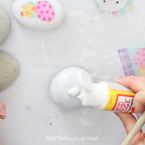 Pouring Mod Podge onto painted rocks.