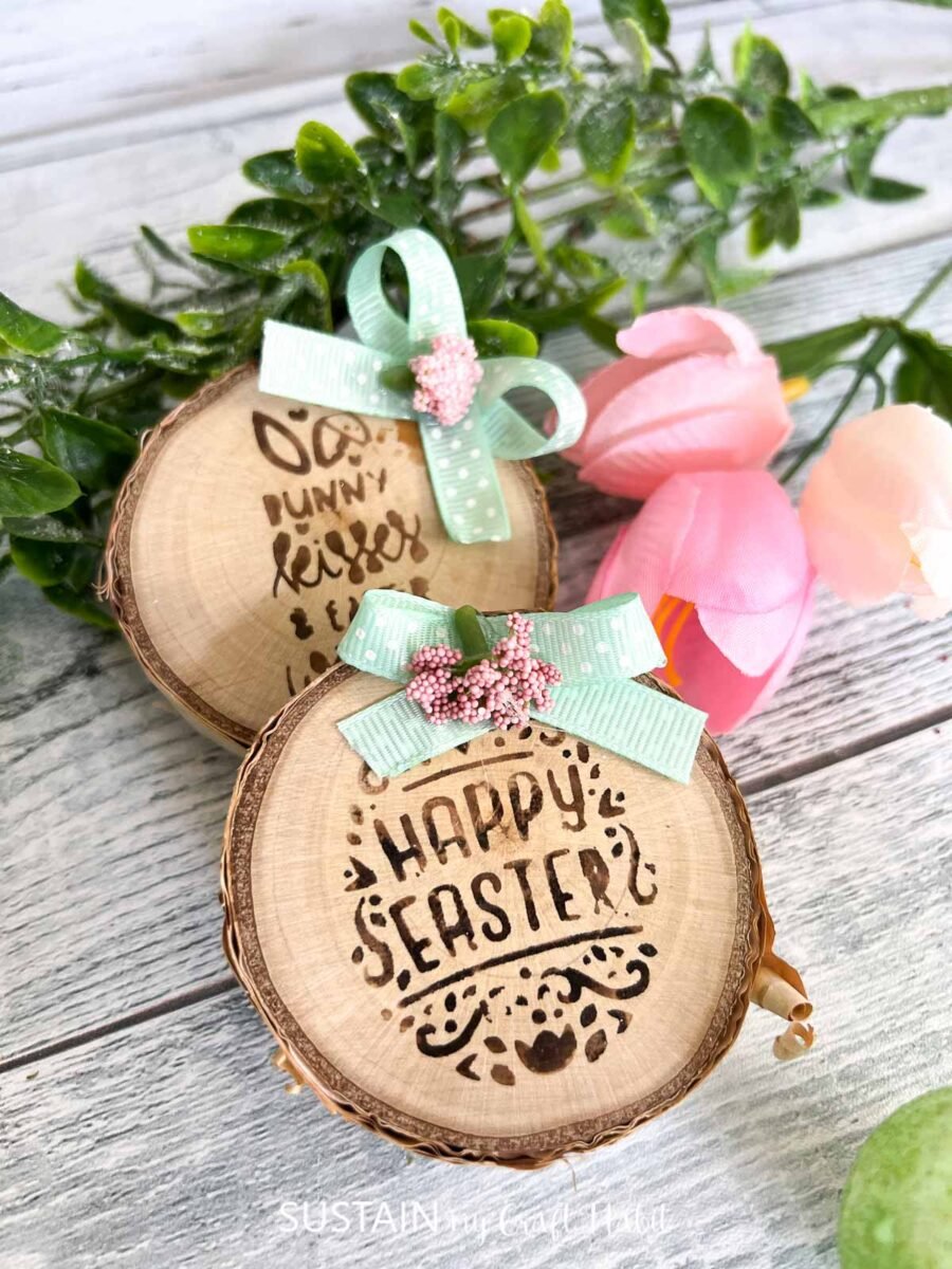 Wood slice with lettering made using a wood burning pen stacked together next to faux flowers.