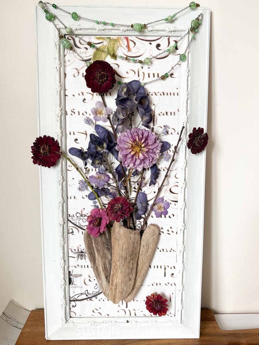 Art encadré fait de fleurs séchées, de papier décoratif et de bois flotté.