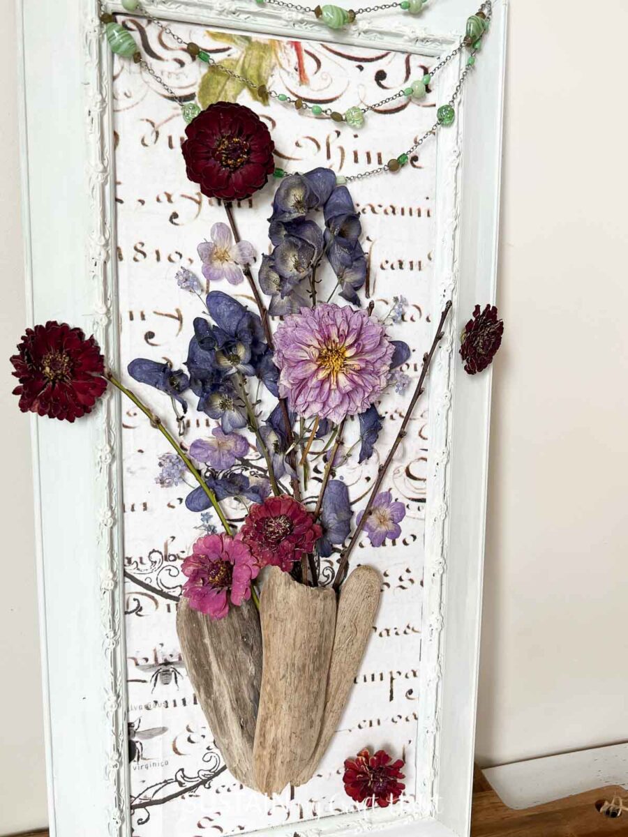 Art encadré fait de fleurs séchées, de papier décoratif et de bois flotté.