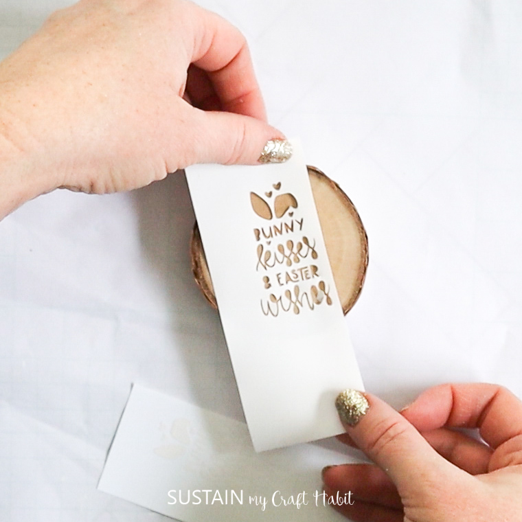Sticking removable vinyl with lettering onto a wood slice.