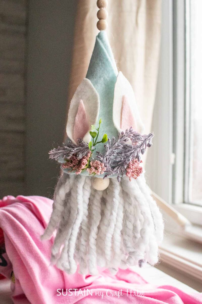 Hanging bunny gnome ornament with wooden beads and decorative flowers on the hat.