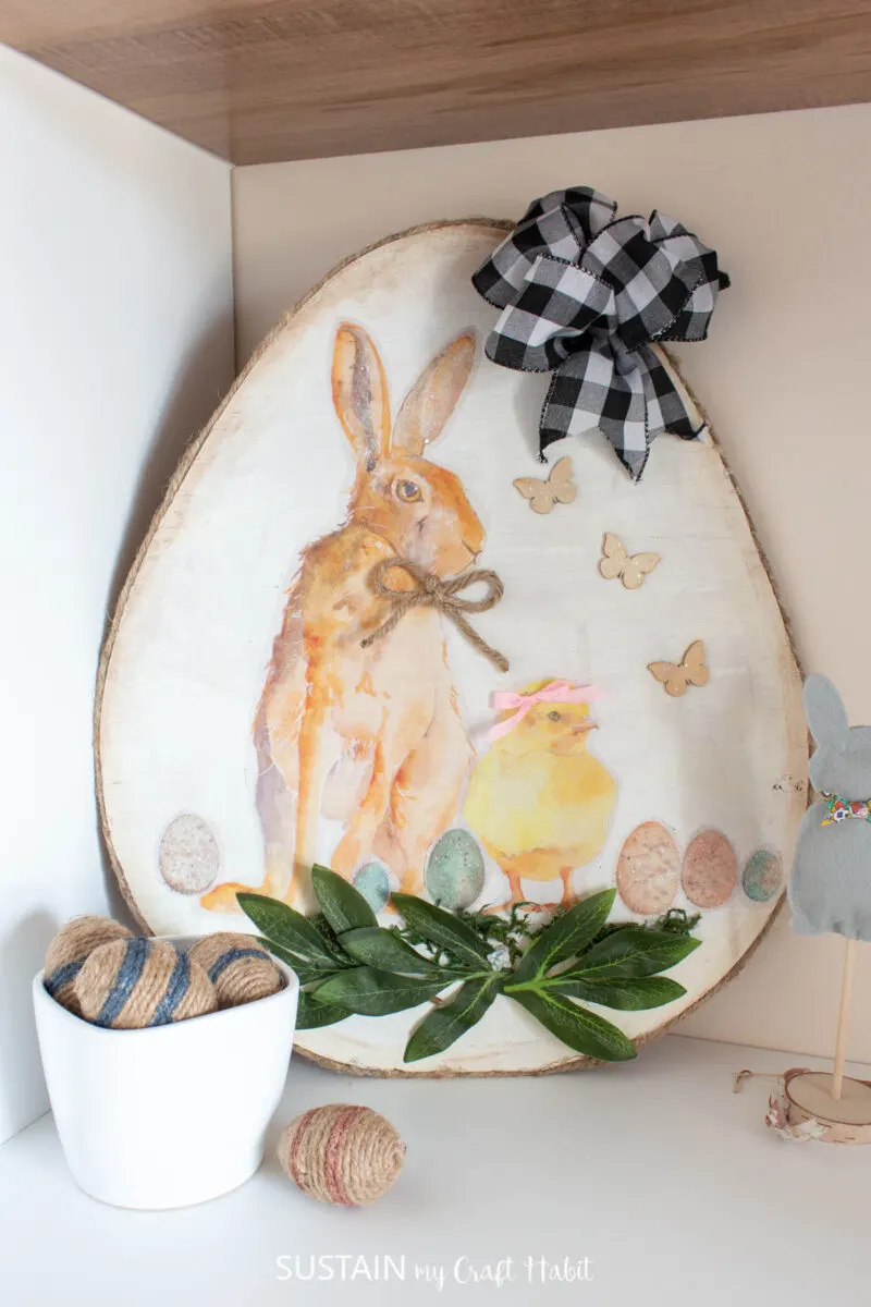 Large Easter egg cutout sign placed in a shelf with twine wrapped eggs and a felt bunny.