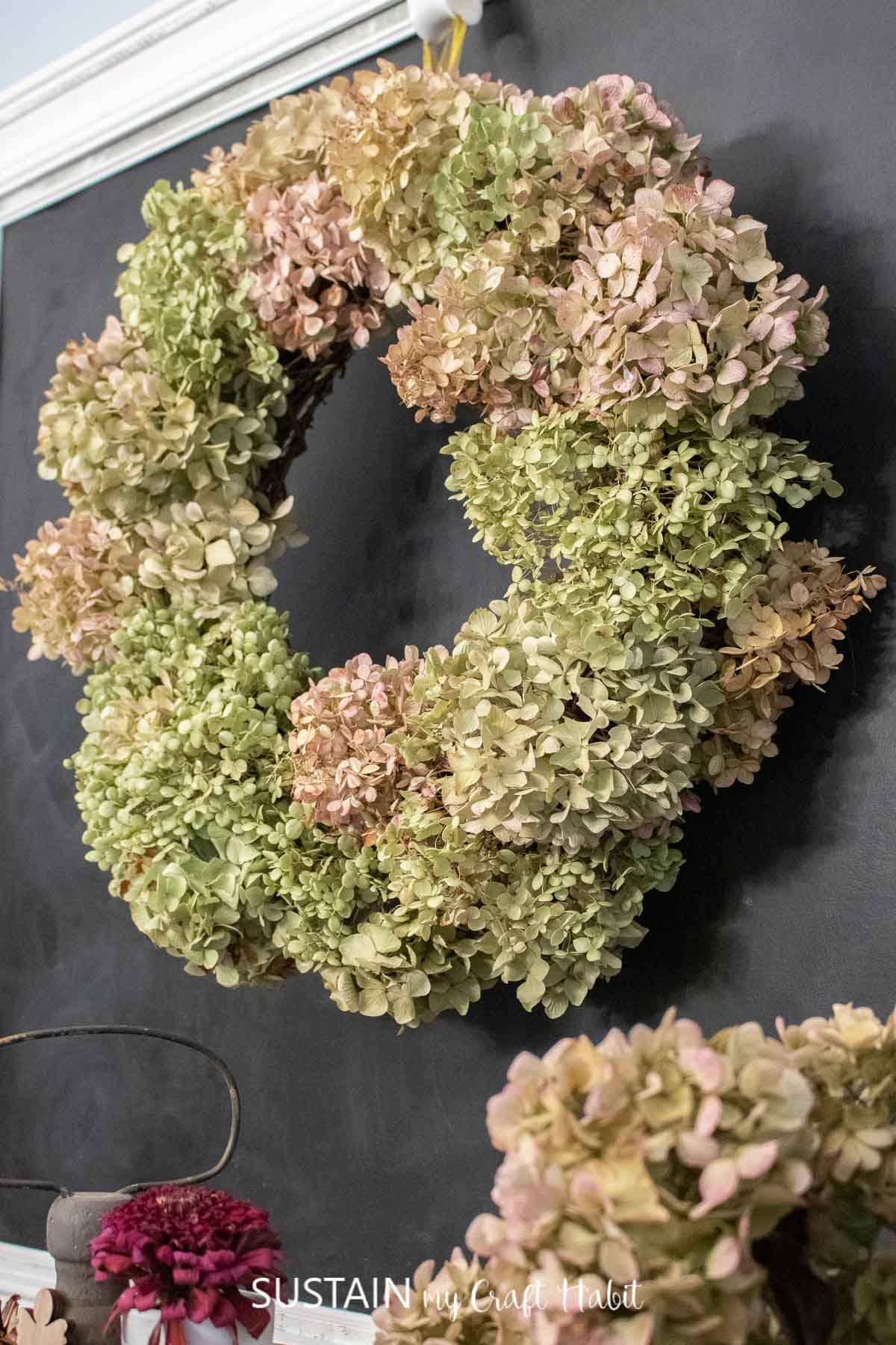 A round wreath made of dried hydrangeas hanging on a glack wall.