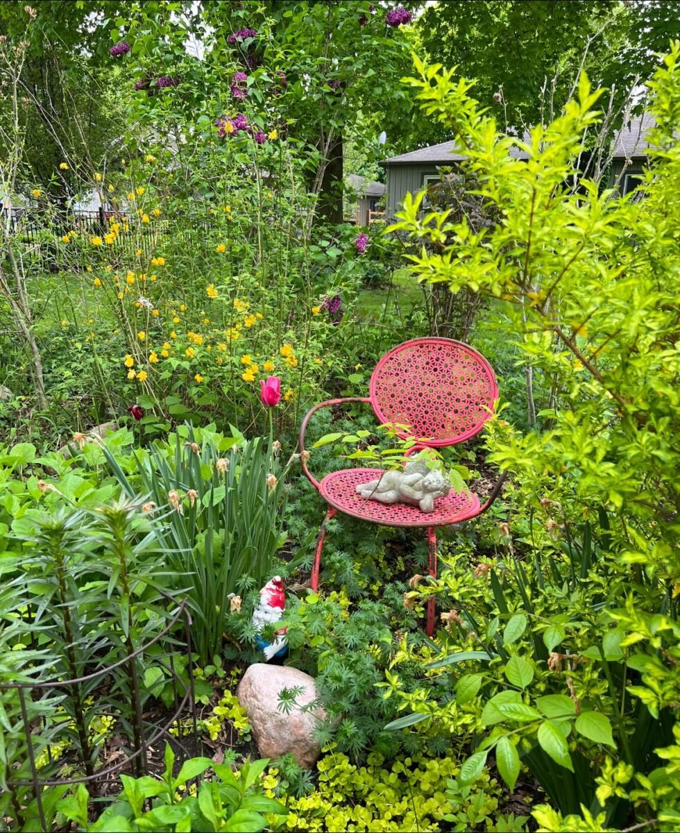 An old red metal chair upcycled as decor for a lush green garden.