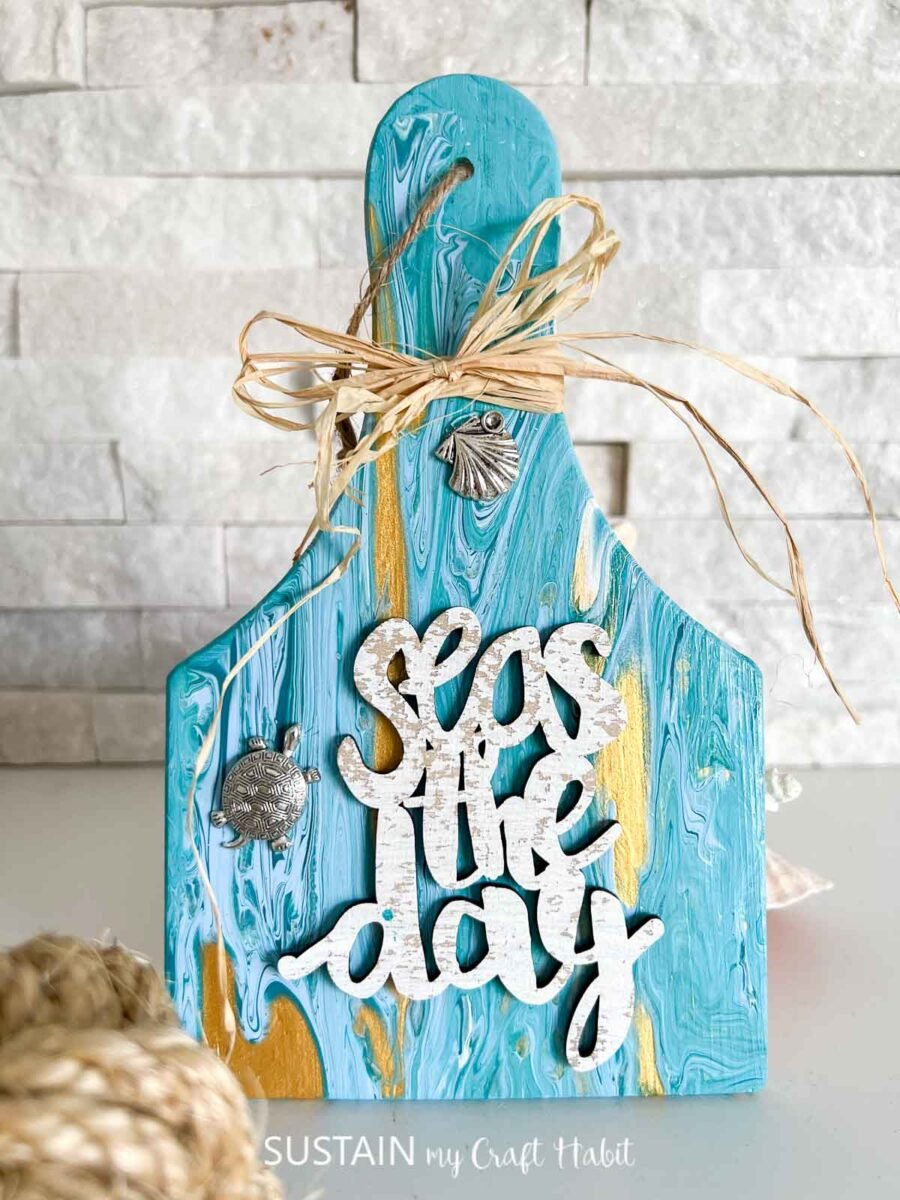 Paint poured wood paddle with beach themed embellishments and ribbon.