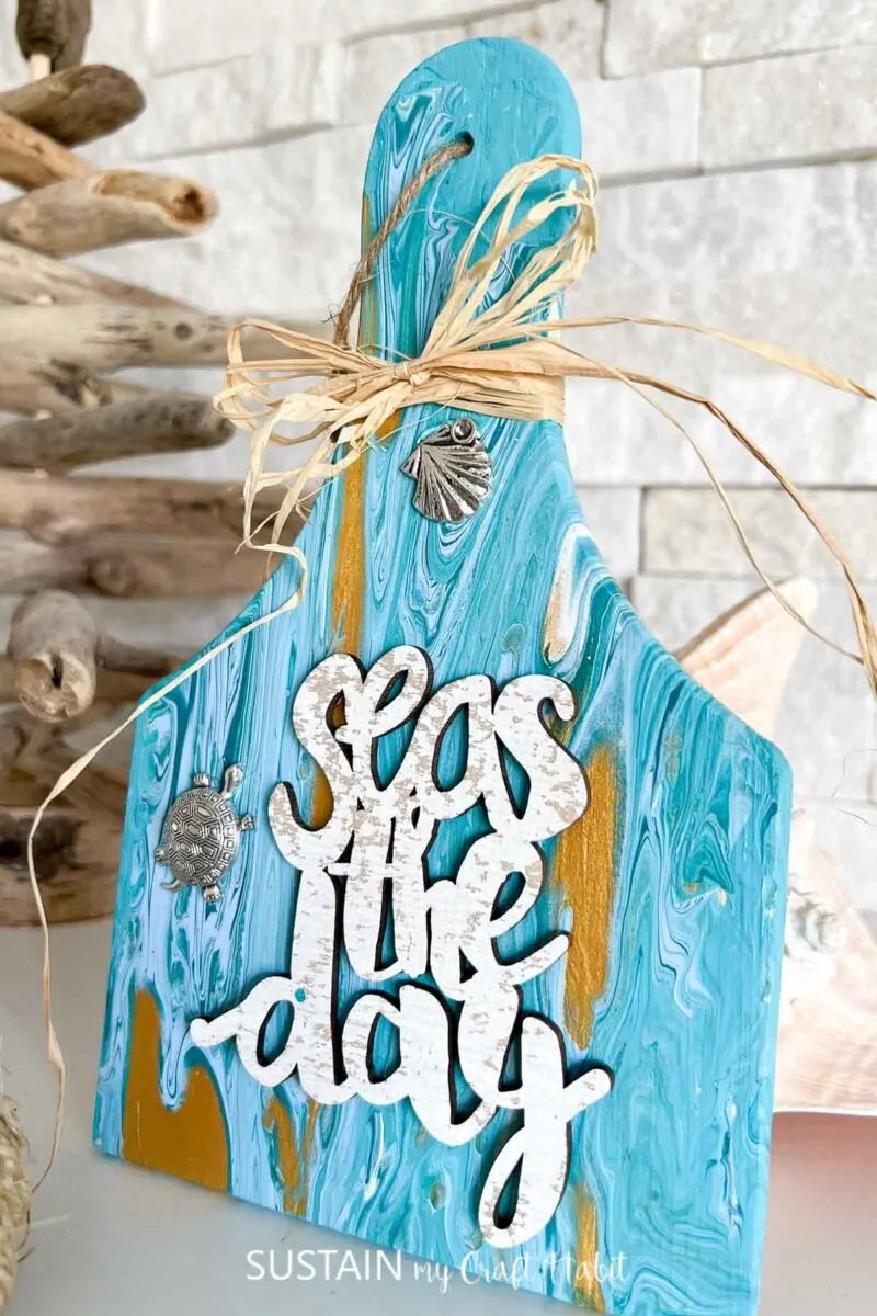 Paint poured wood paddle with beach themed embellishments and ribbon.