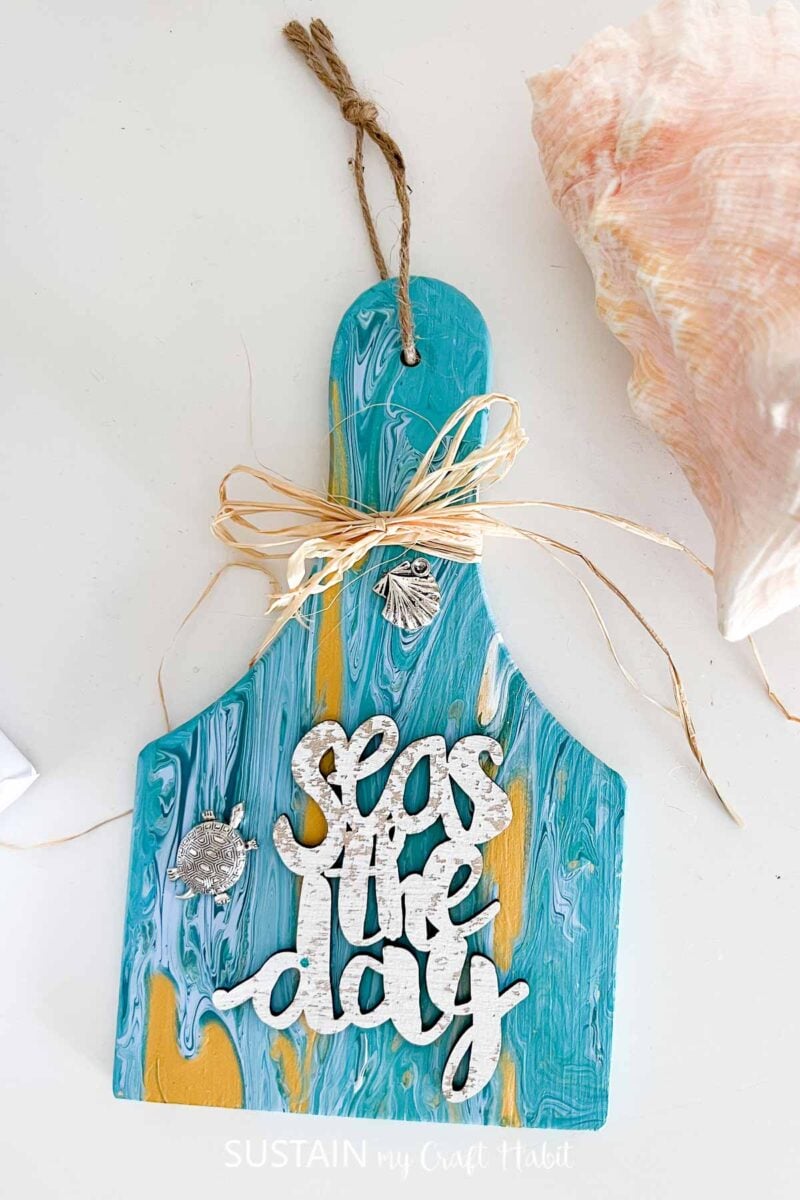 Paint poured wood paddle with beach themed embellishments and ribbon.