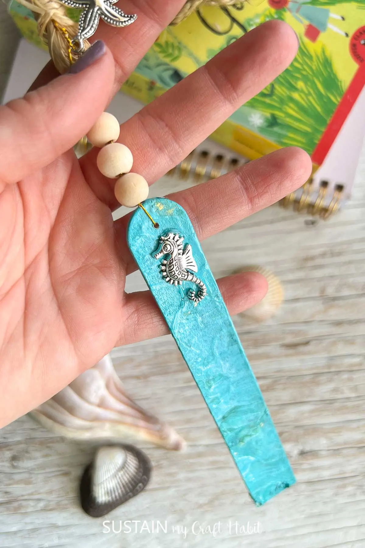 Hand holding a finished paint poured beachy bookmark.