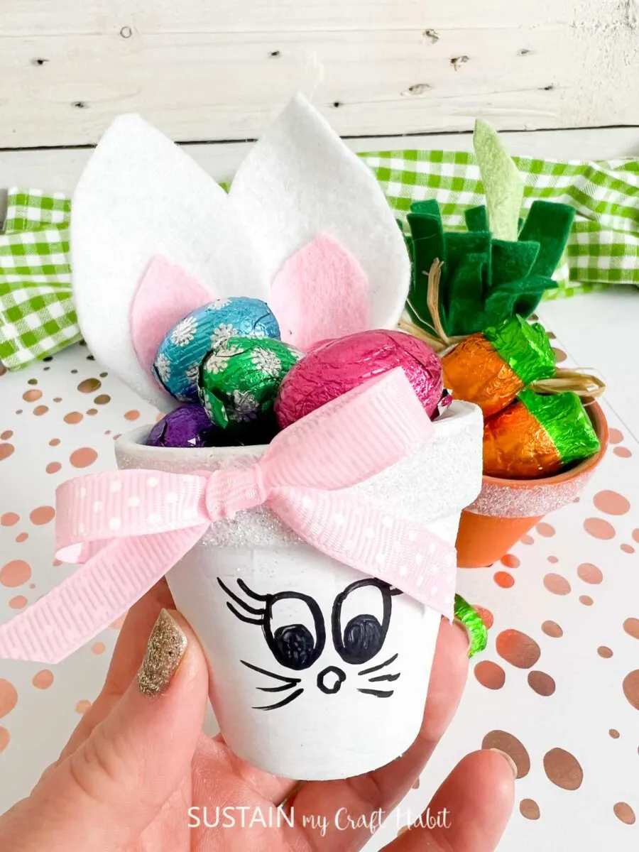 Hand holding a Clay pot Easter bunny with a pink bow and filled with candy.