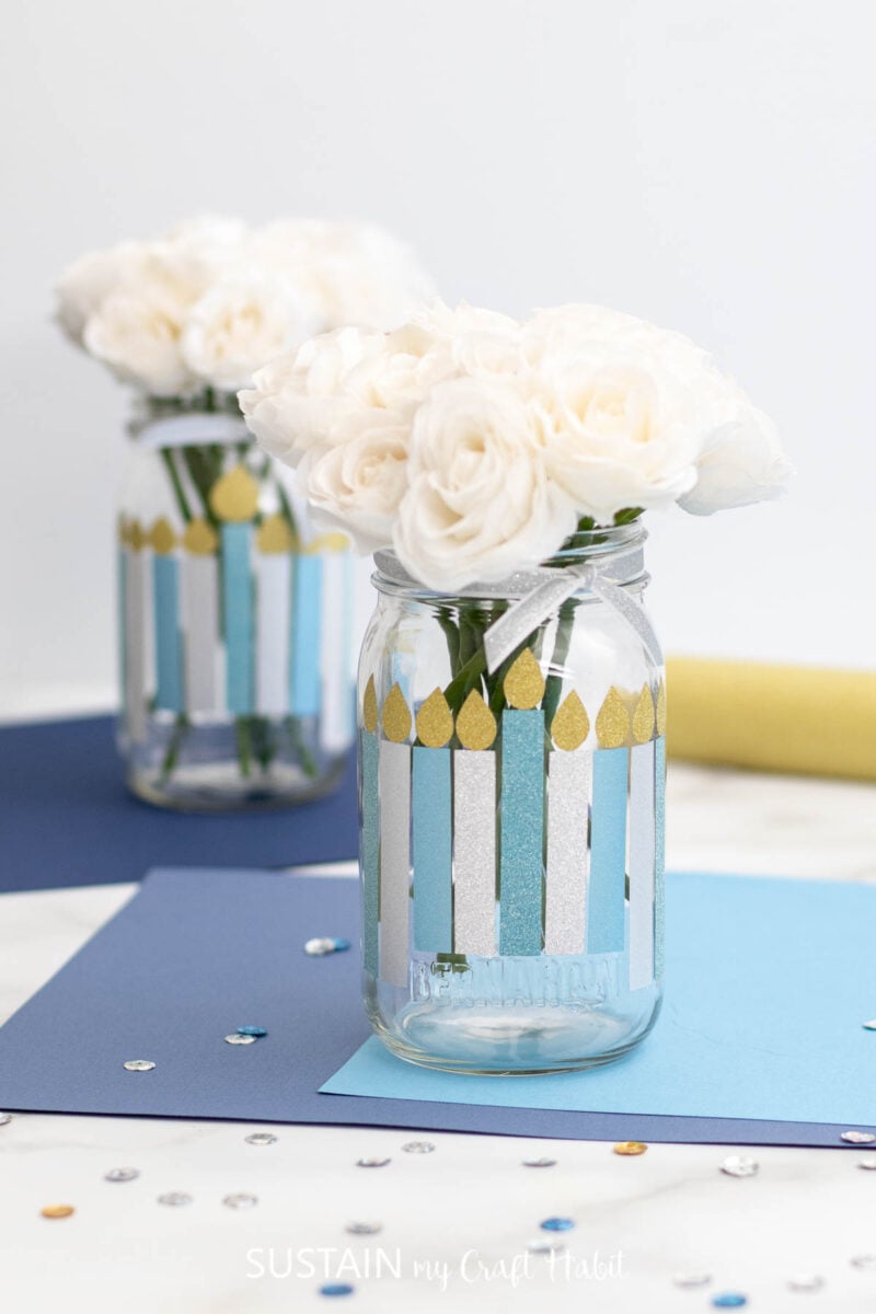 Hanukkah decorations on glass jars made with vinyl flames, ribbon and faux flowers.