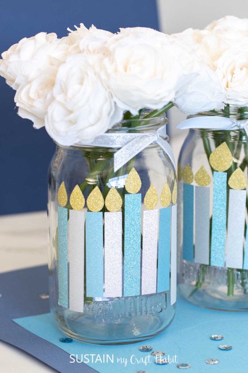 Hanukkah decorations on glass jars made with vinyl flames, ribbon and faux flowers.