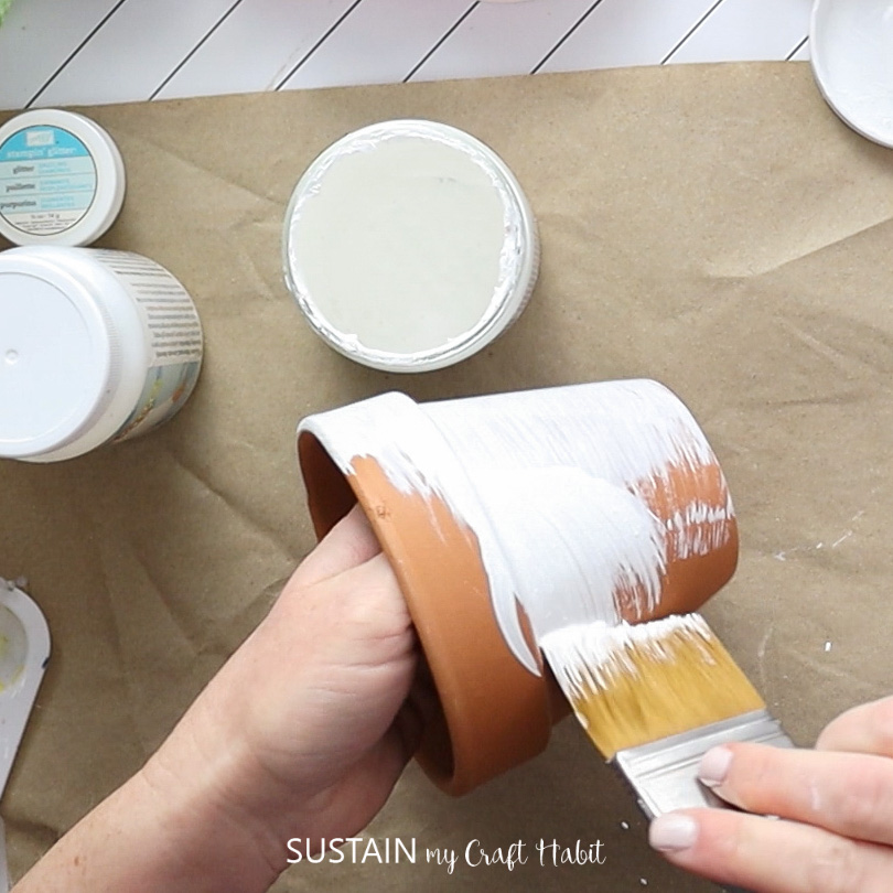 Painting a clay pot with white paint.