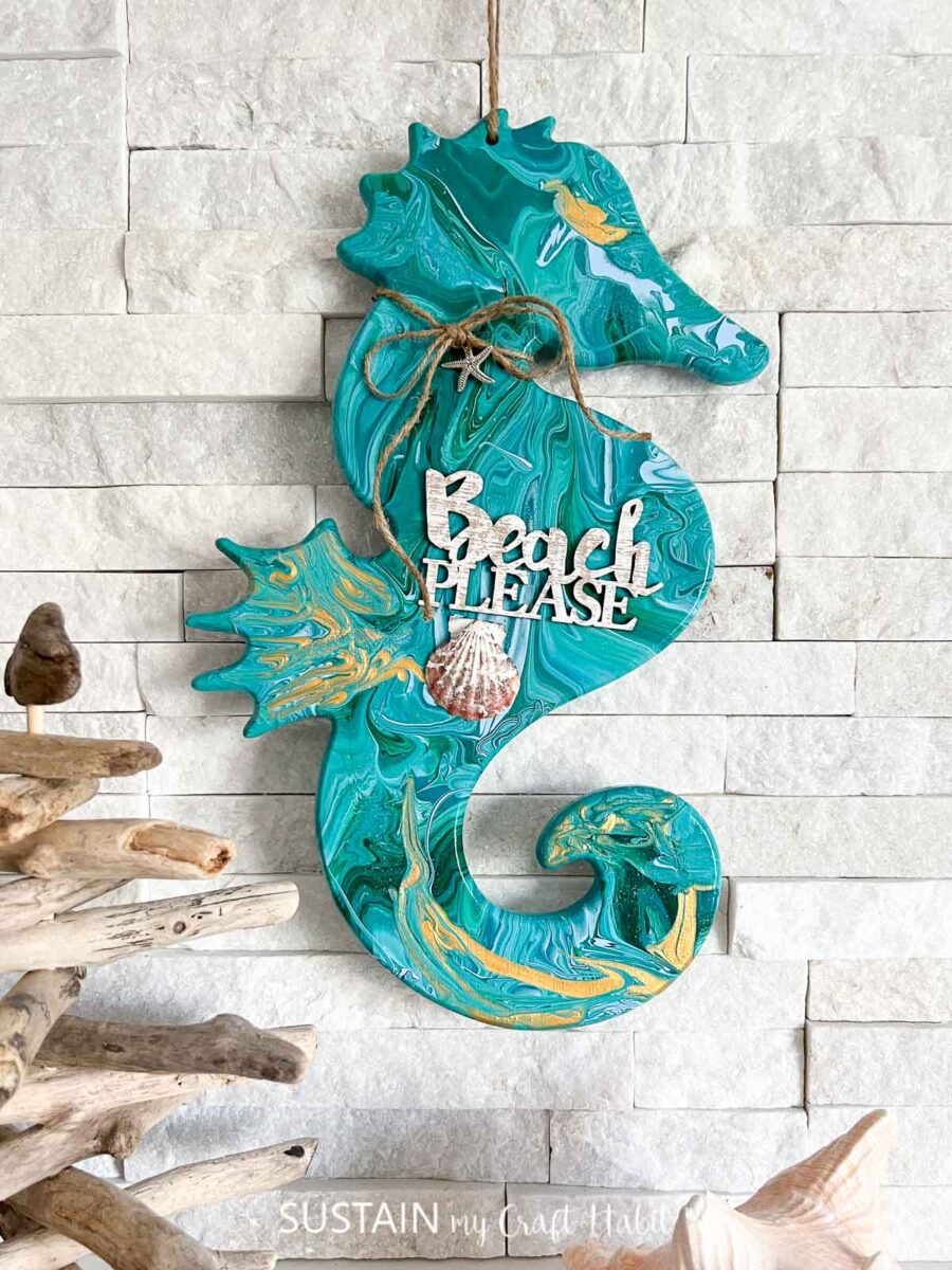 Paint poured wooden seahorse embellished with a wood cut out phrase, twine, charms and a seashell. 