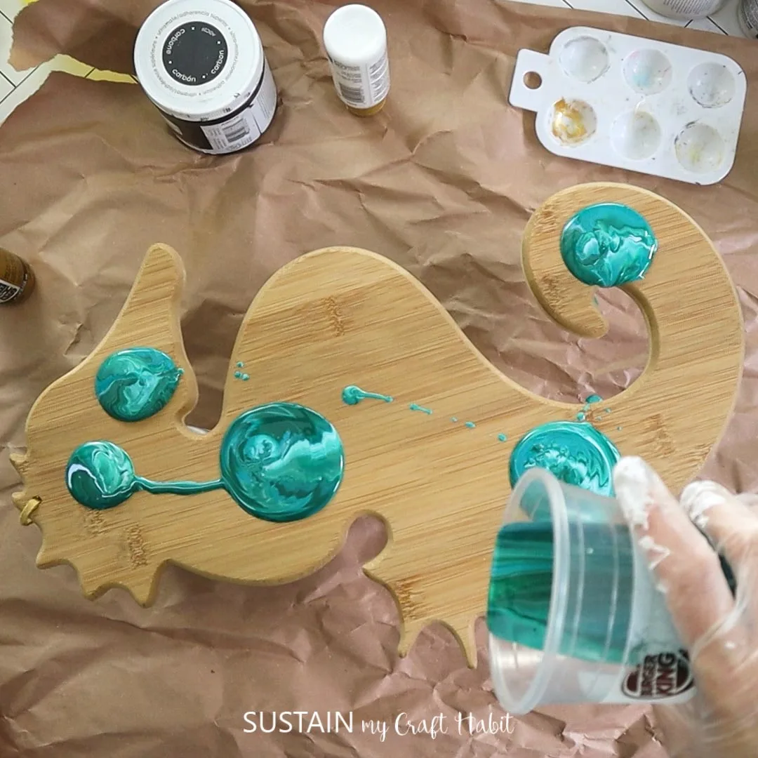 Pouring paint over a wooden seahorse.