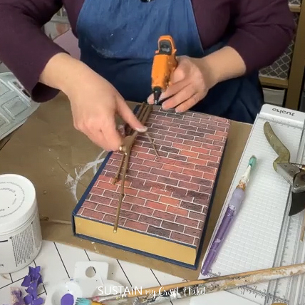 Hot gluing twigs onto an upcycled book.