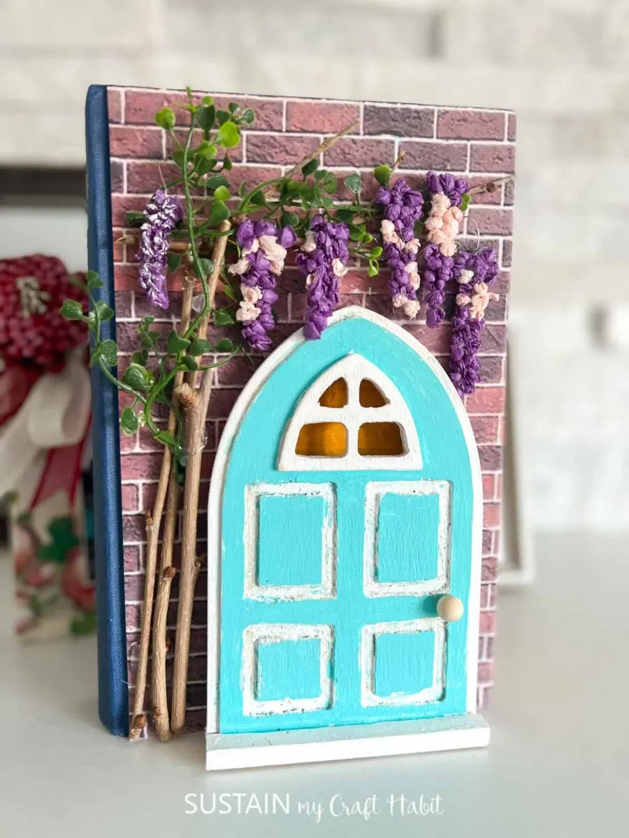 Upcycled book craft with decorative paper, painted wood door, twigs and flowers.