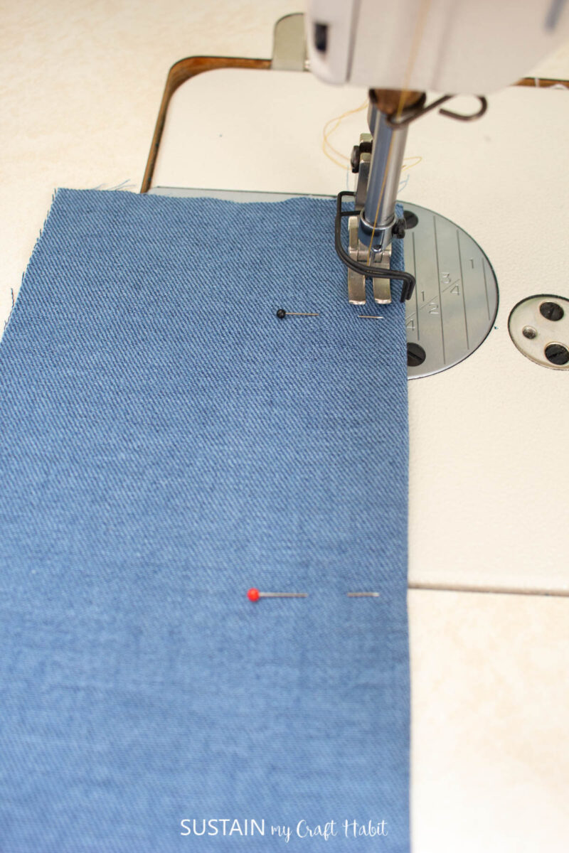 Pins added to the blue fabric and sewing machine sewing a seam. 