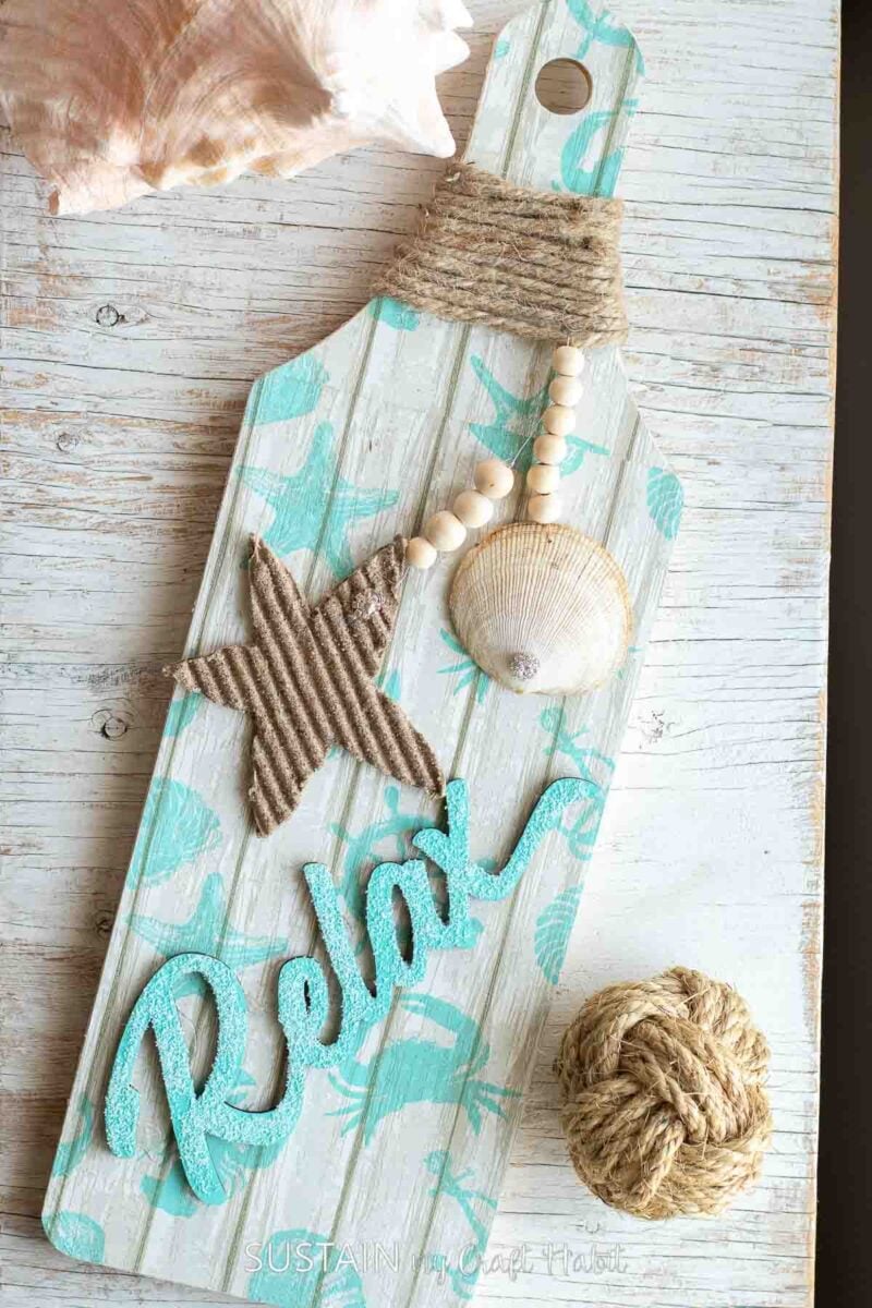 Beach themed wood panel decorated with a relax sign, twine, shells and stars.