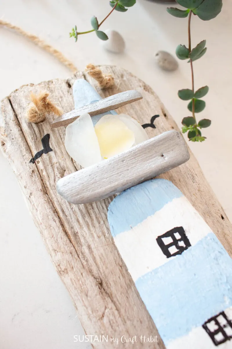 Close up of a coastal lighthouse driftwood craft with rocks, driftwood, sea glass, twine and paint.